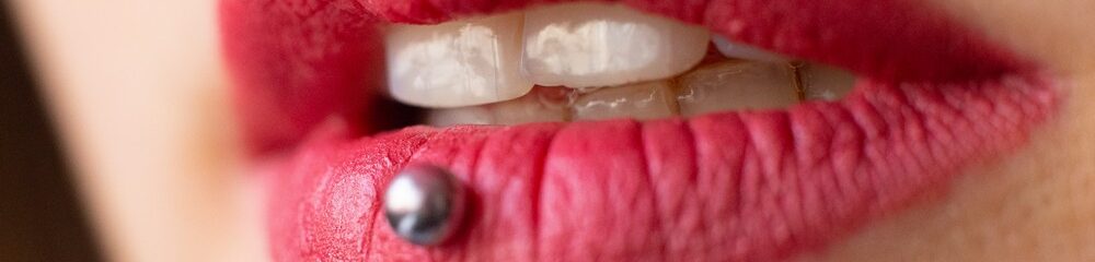 Close-up of pink lips with a vertical labret piercing and visible teeth.