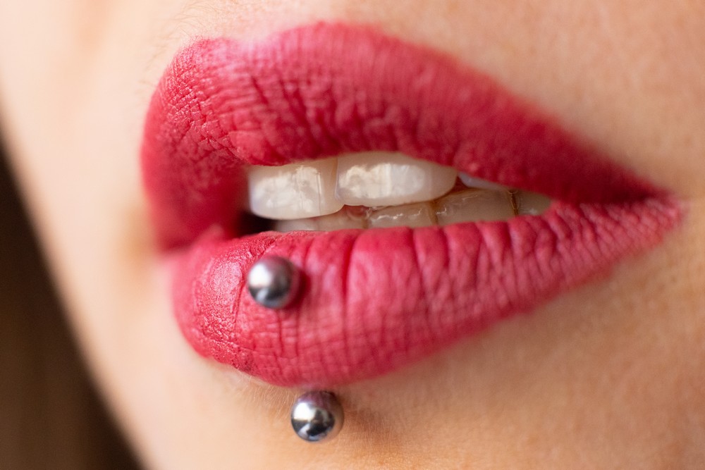 Close-up of pink lips with a vertical labret piercing and visible teeth.
